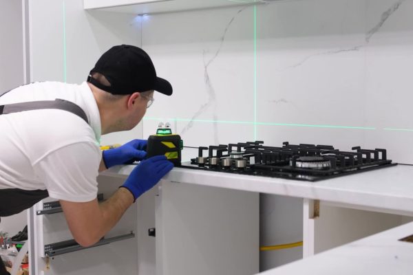 A worker installs a new gas stove and measures with a laser-min